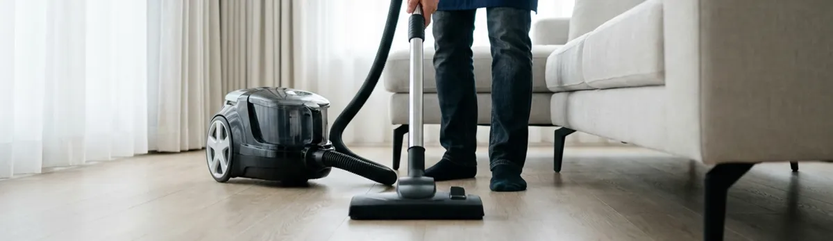 Professional house cleaner vacuuming a living room floor with a canister vacuum cleaner, Shreveport, LA.